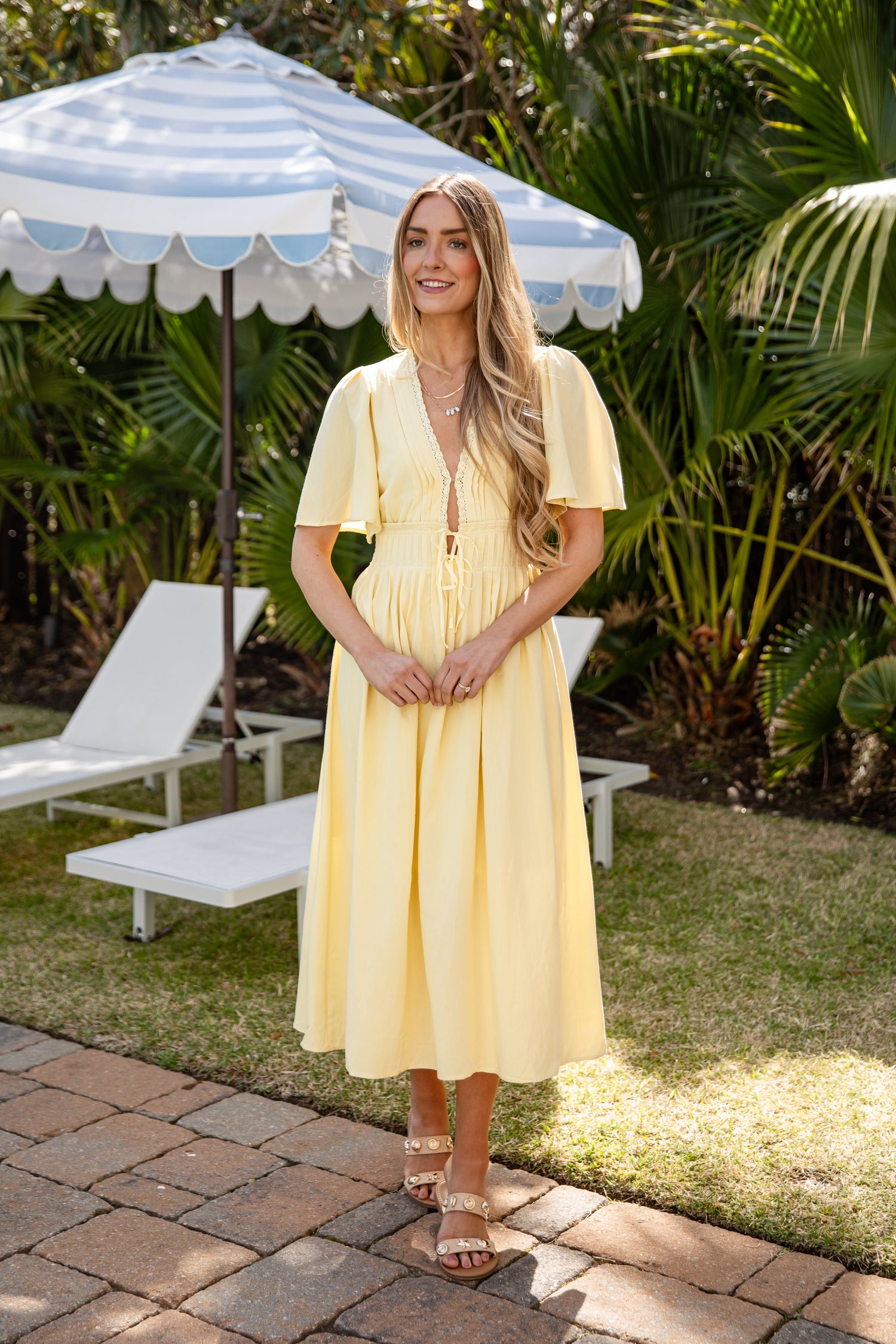 Woman in a yellow dress standing under a striped umbrella in a garden setting