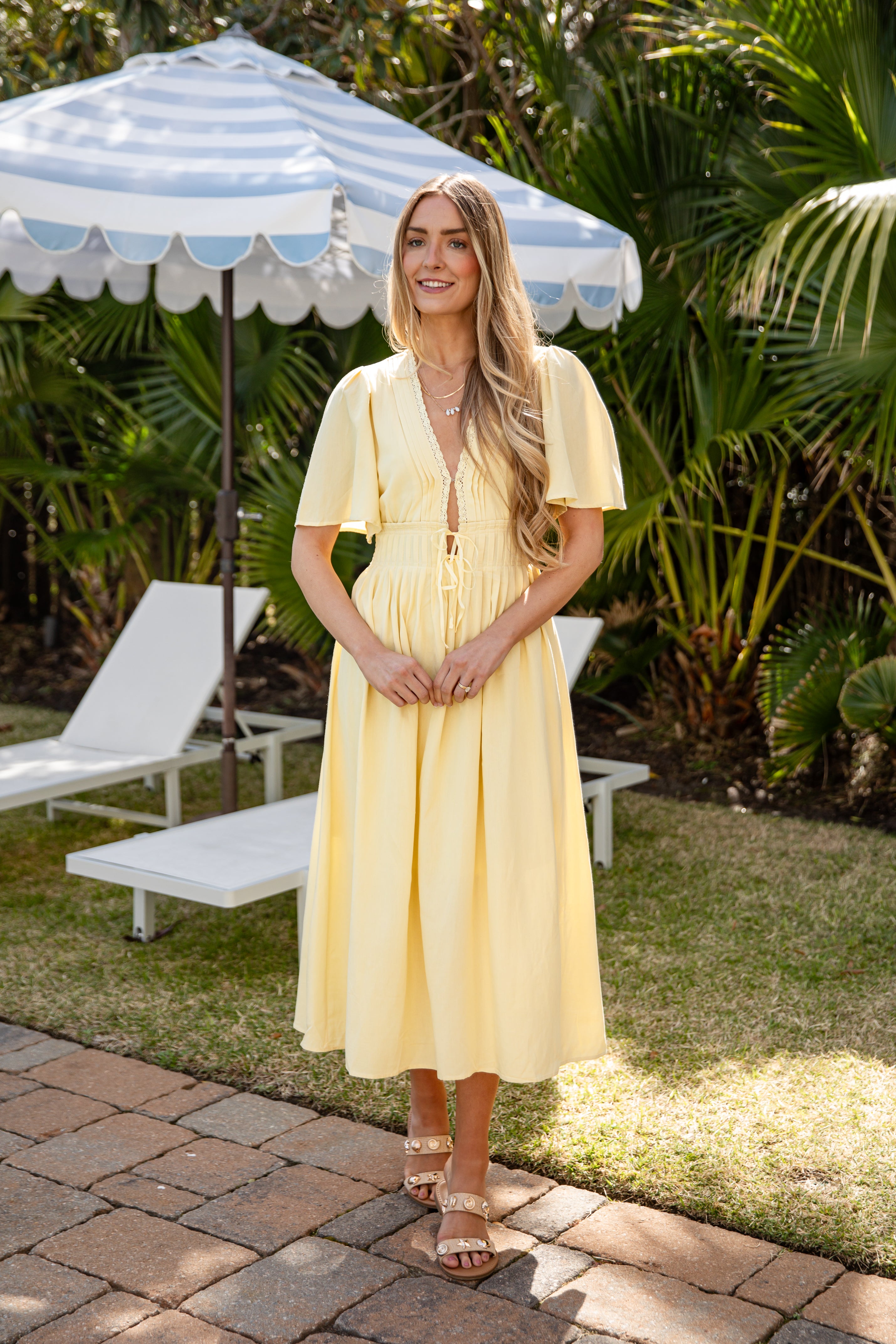 Woman in a yellow dress standing under a striped umbrella in a garden setting